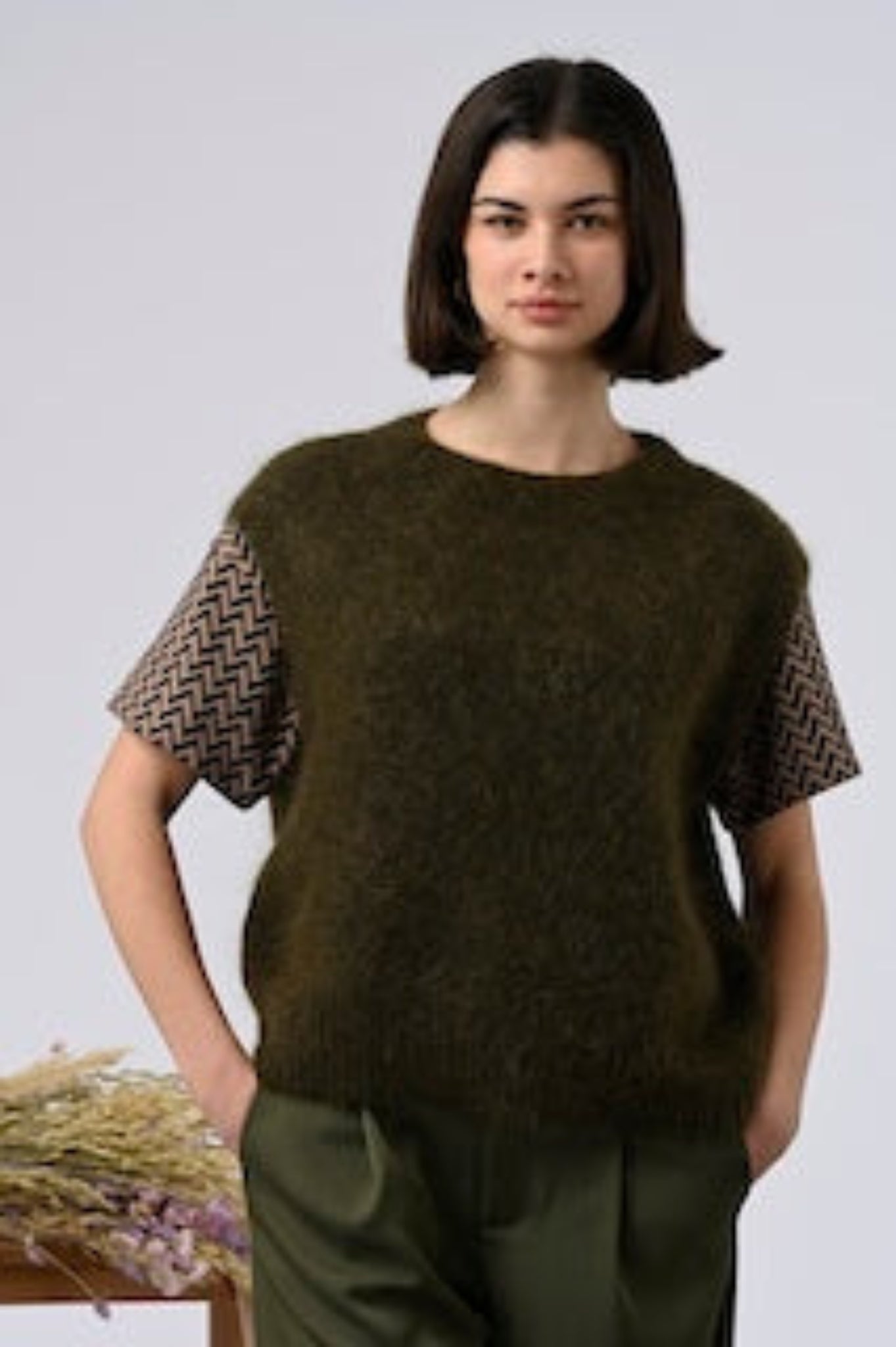 woman wearing minimalist khaki green sweater vest styled over patterned top