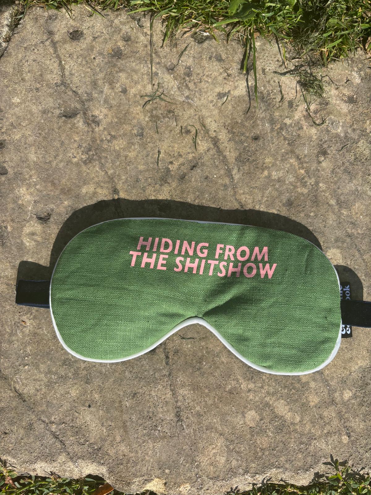 Relaxing lavender-filled eye mask from Caroline Colebrook. Green linen with pink lettering saying "hiding from the shitshow" 