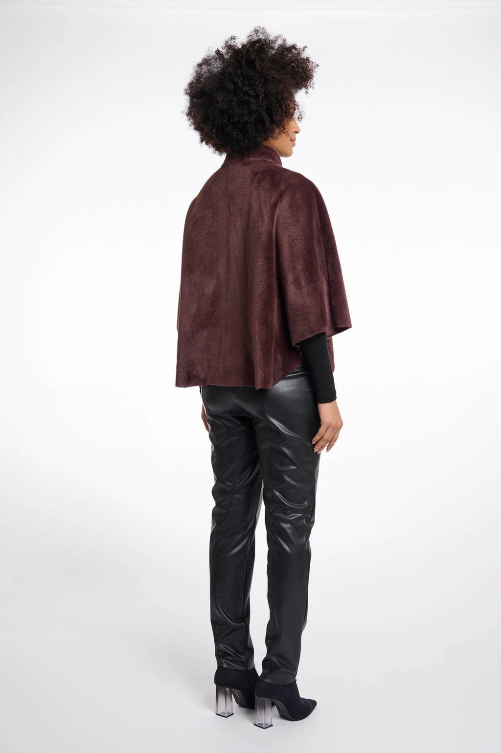 Person wearing a chocolate brown faux fur cape and black pants on a white background