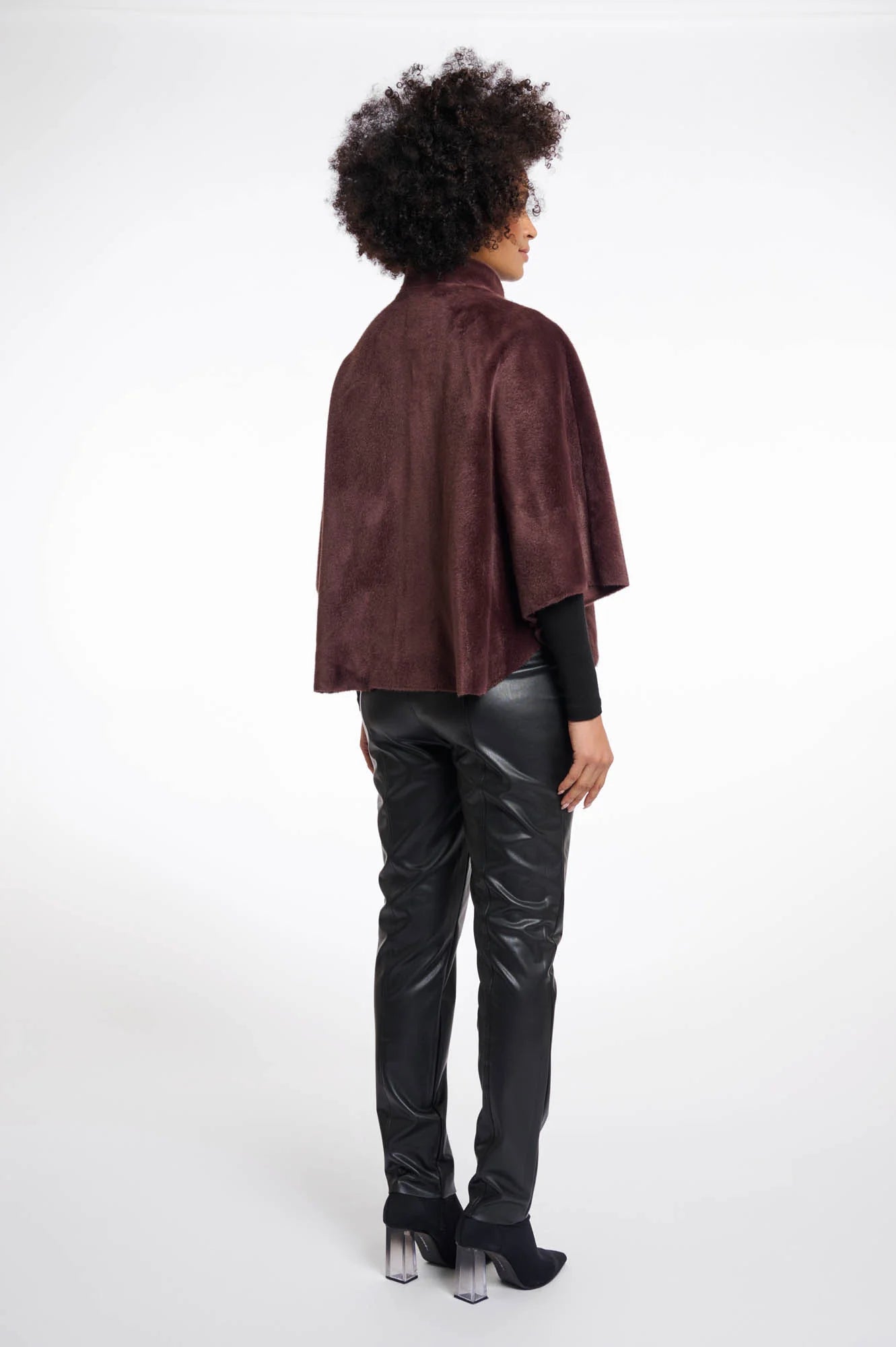 Person wearing a chocolate brown faux fur cape and black pants on a white background