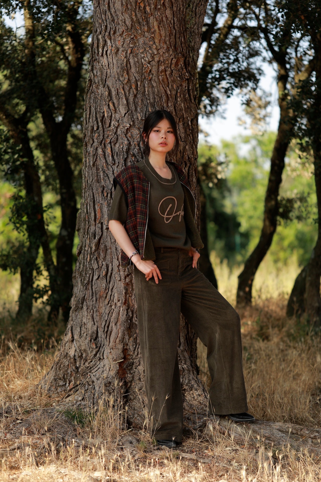 woman leaning against a tree wearing flattering high-rise khaki trousers for everyday styling