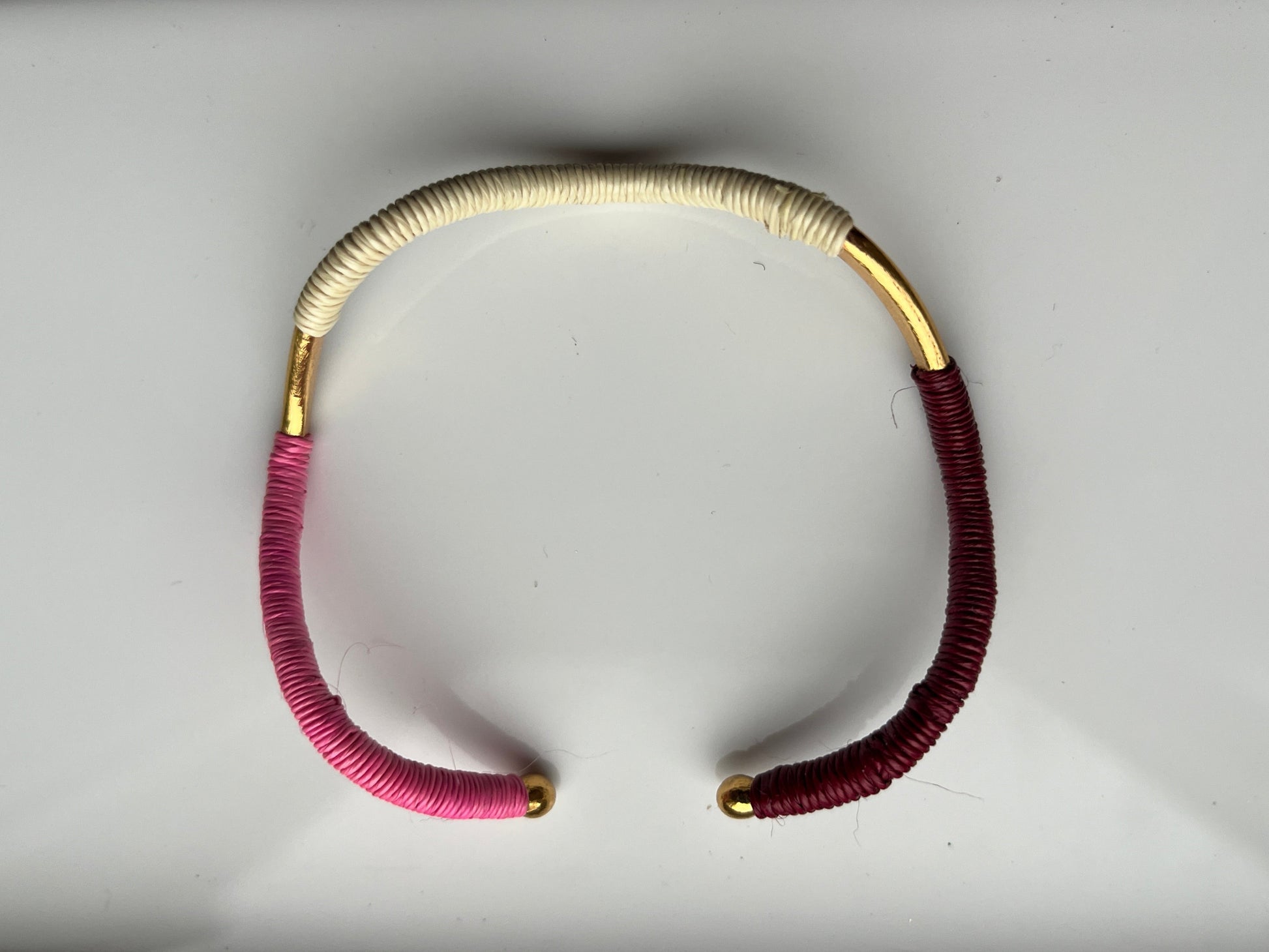 Wavy bangle bracelet  with pink, gold, and ecru strands on a light gray background