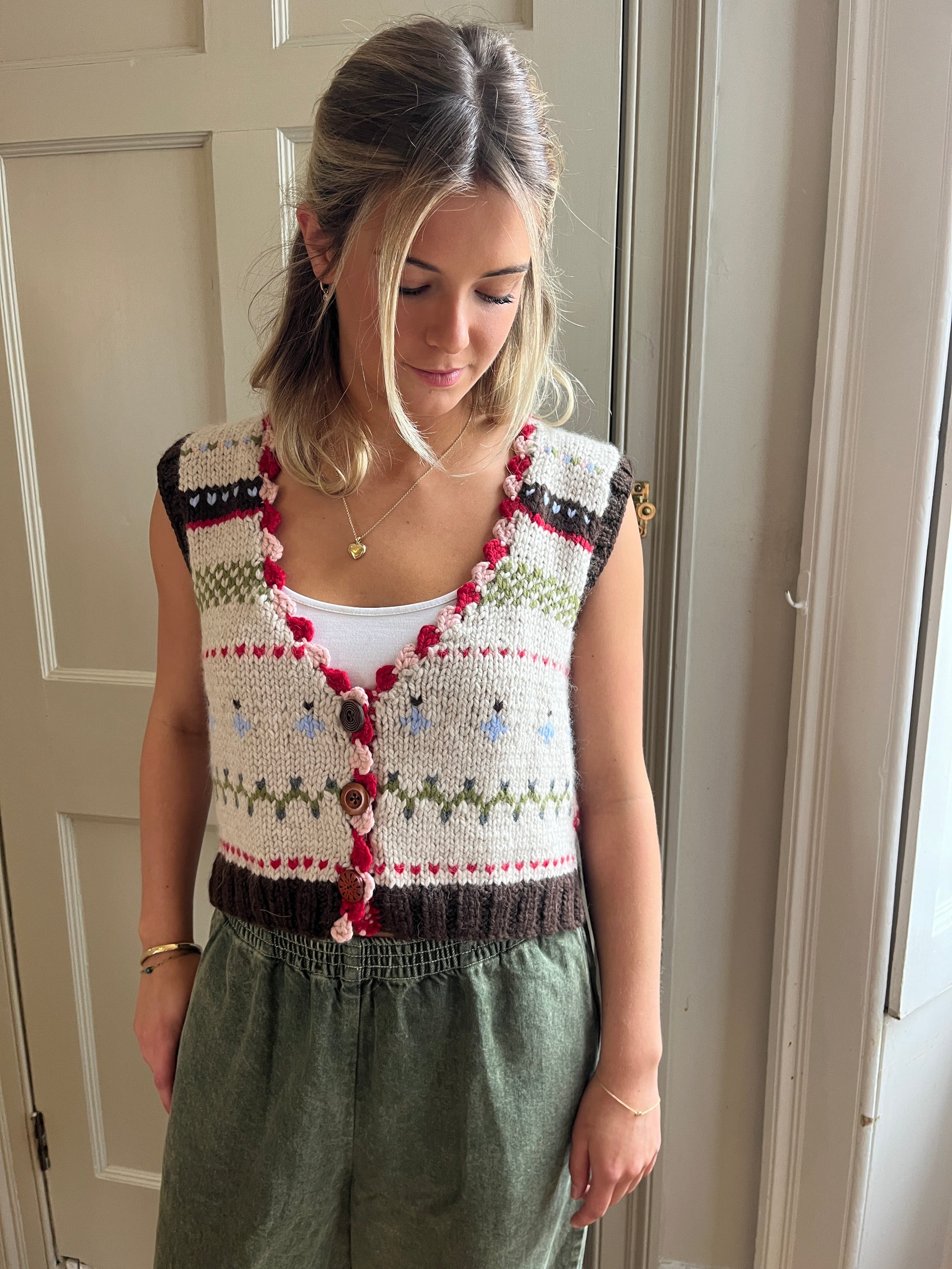 Woman wearing a colorful nicky dupont hand-knitted waistcoat  over a white top, standing against a neutral background.