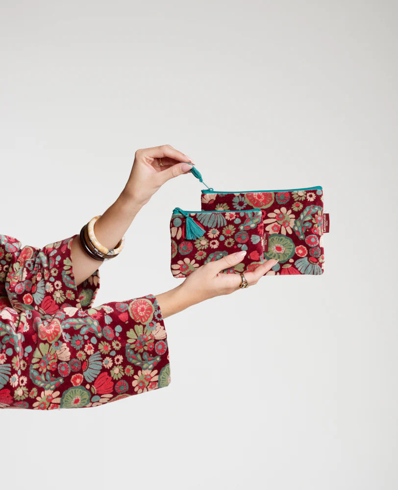 Person holding a floral-patterned Les Touristes velvet pouch against a plain background