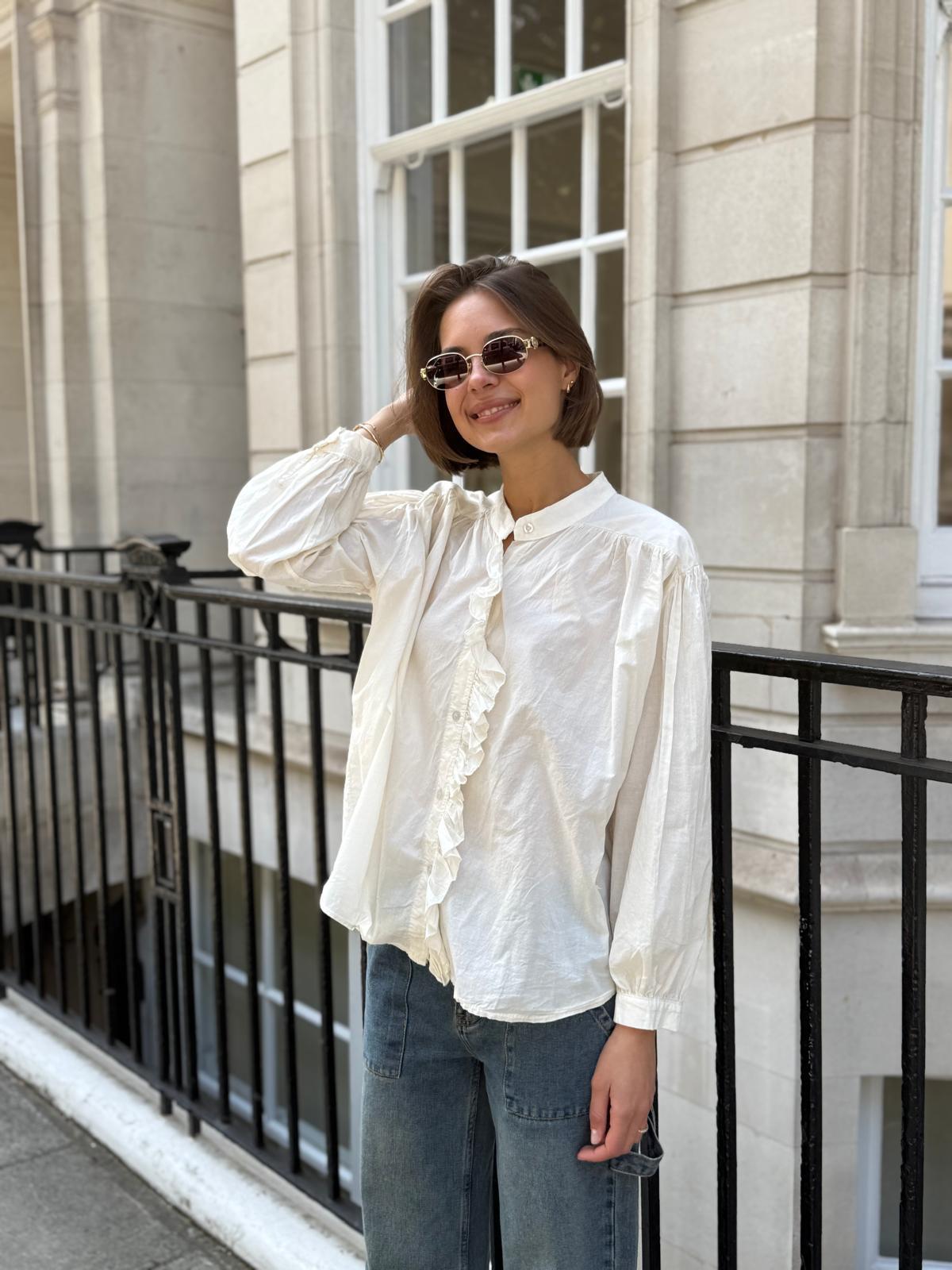 Women’s cream blouse with frill detailing on collar and cuffs shown on model with jeans