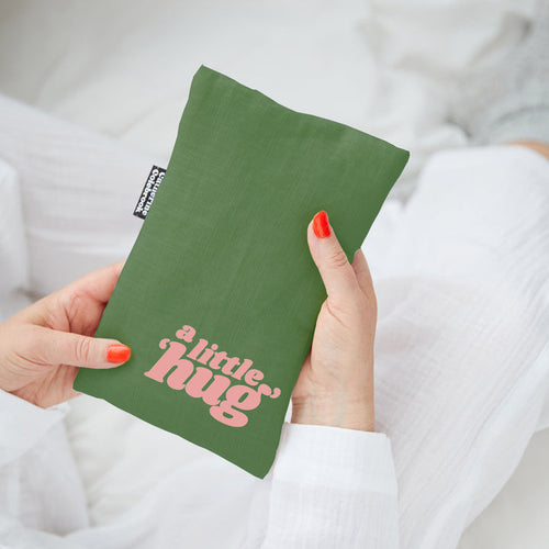 Green linen mini hot water bottle with 'a little hug' text held by a person wearing a white shirt.