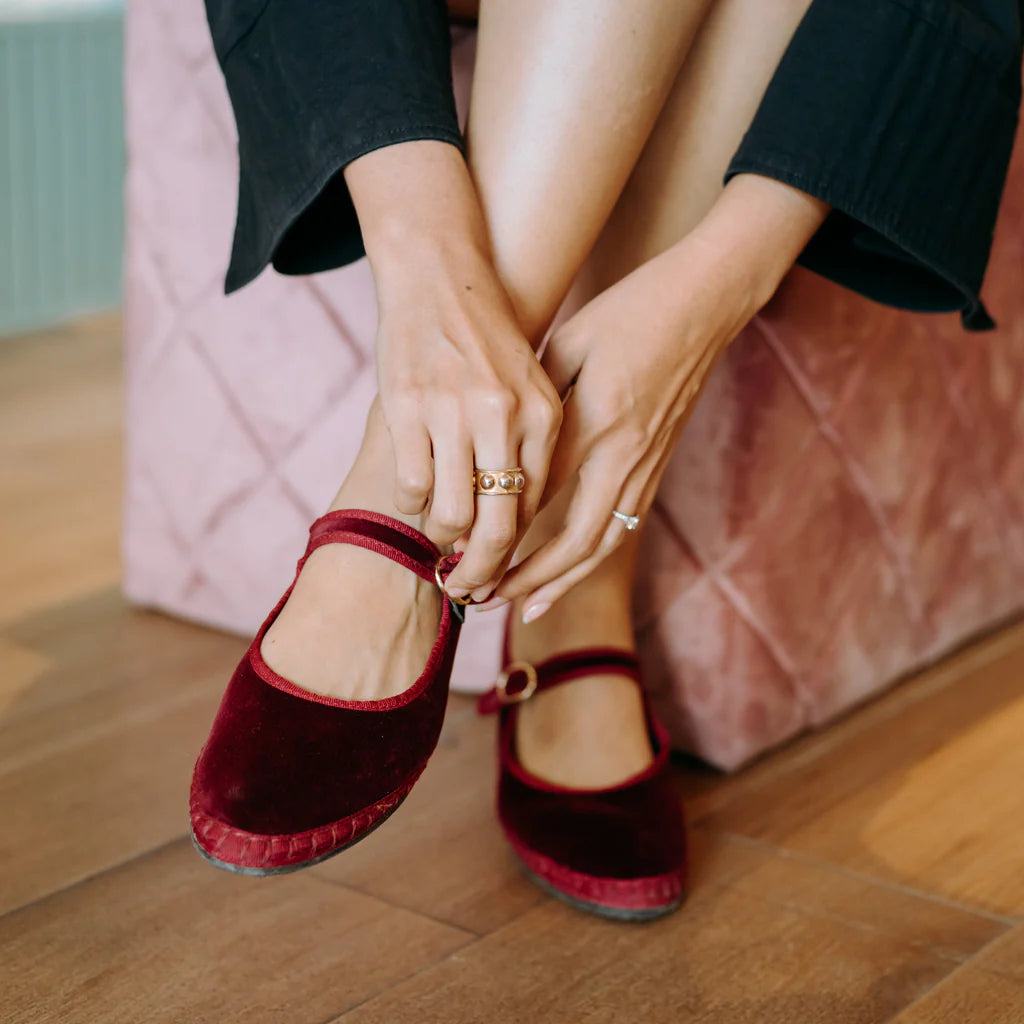 Flabelus burgundy velvet Mary Jane with buckle strap worn by model sitting on pour